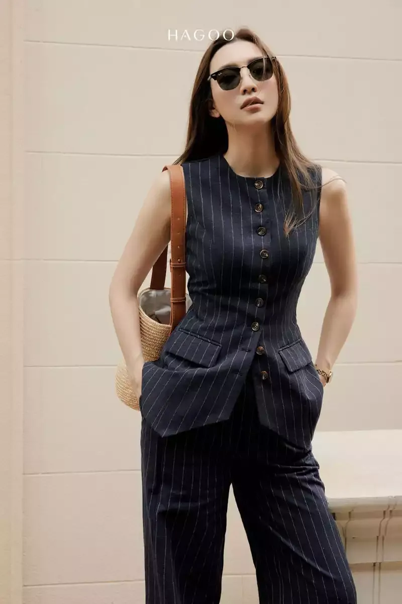 Một người mẫu mặc áo vest gile nữ dáng ngắn màu trắng kem, phối cùng quần âu đồng bộ và túi xách hàng hiệu, tạo phong cách thời thượng và đẳng cấp, thể hiện xu hướng thời trang hiện tại.