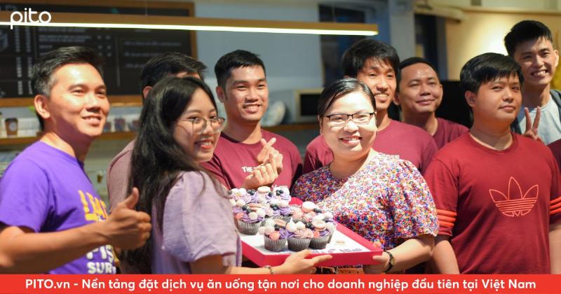 Một nhóm đồng nghiệp đang vui vẻ chúc mừng sinh nhật tại văn phòng, trên bàn có bánh kem và bóng bay. Lời chúc thể hiện sự chuyên nghiệp và gắn kết.