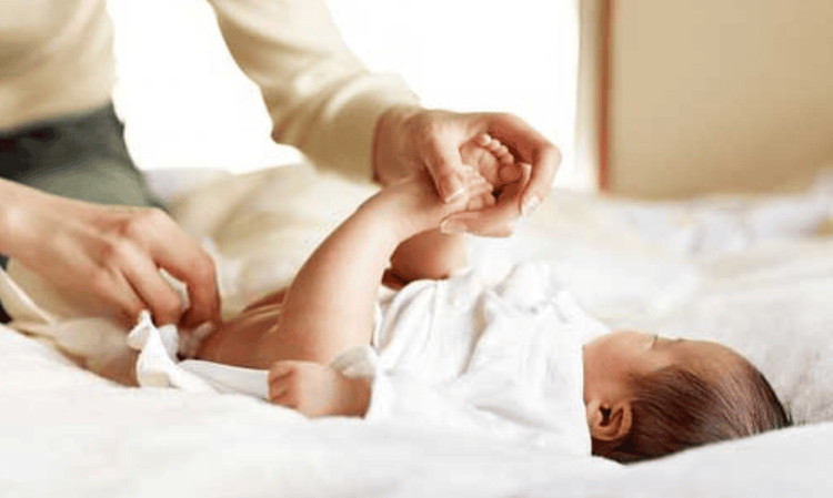 Bàn tay người lớn đang thoa kem lên mông em bé, nhấn mạnh việc dưỡng ẩm sau mỗi lần thay tã để phòng ngừa hăm tã